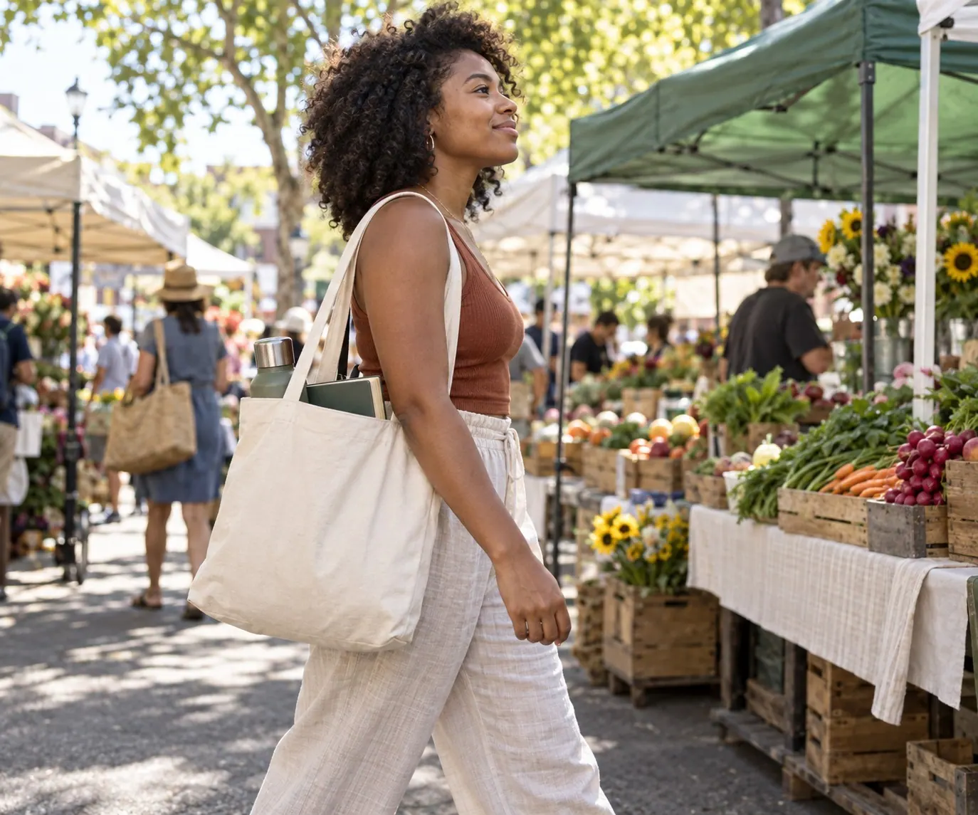A person carries a canvas tote with a book and water bottle through a neighborhood market.