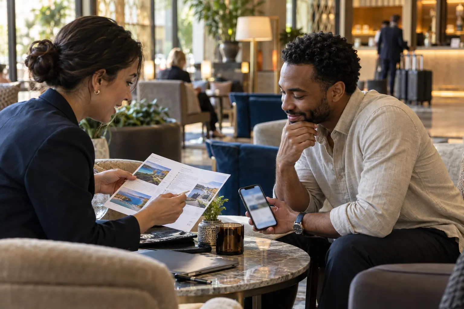 A travel advisor and client review printed hotel options in a hotel lounge; the client holds a smartphone.